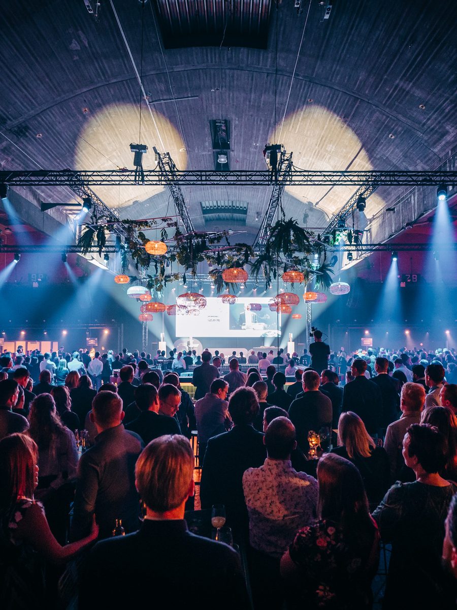 Volle zaal tijdens het nieuwjaarsevent van DEME, met lichtbundels en hangende lampions boven het podium